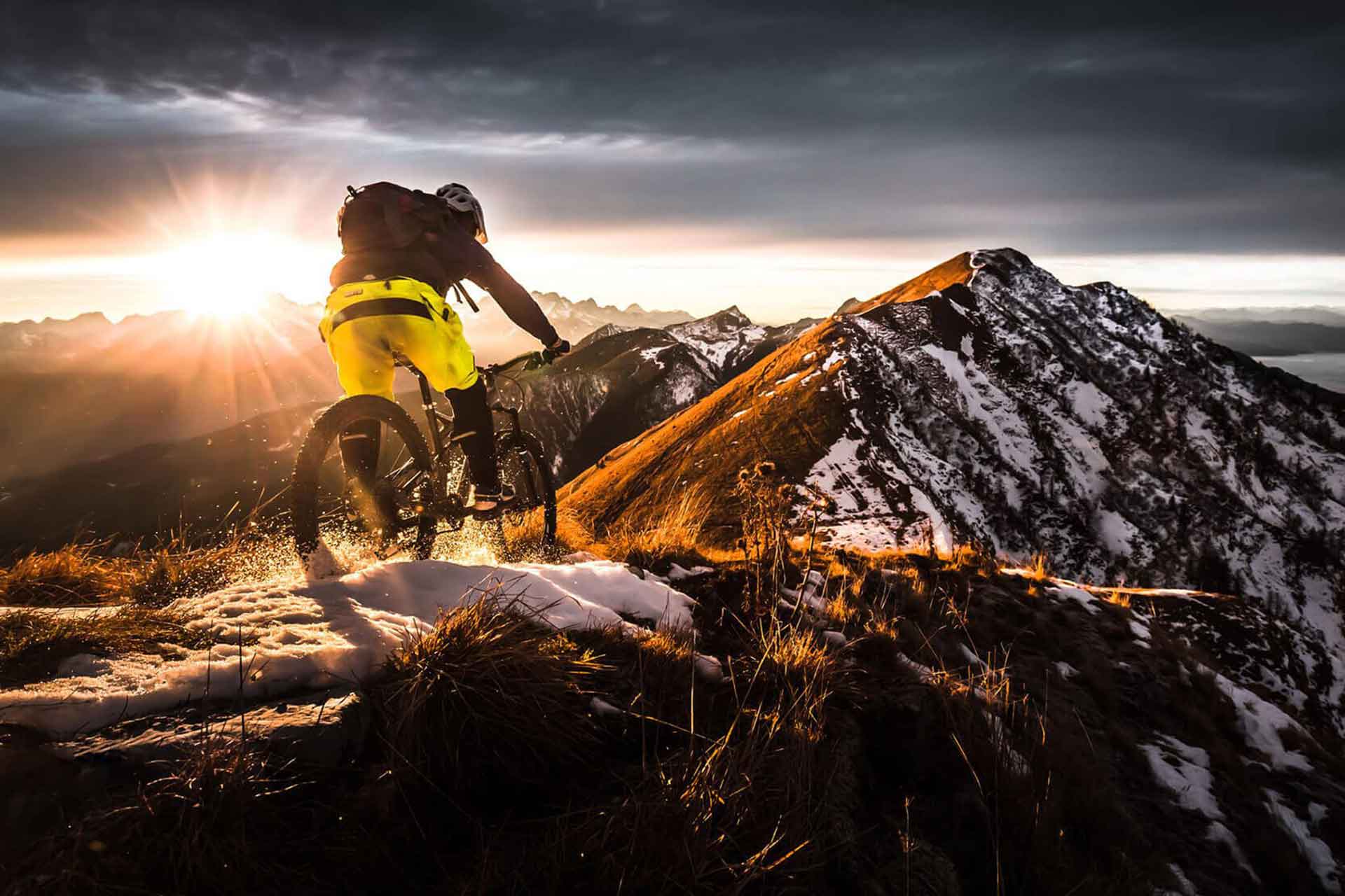Mountain biker riding a snowy ridge into a golden sunrise
