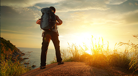 Hiker with a pack watching sunrise from a summit